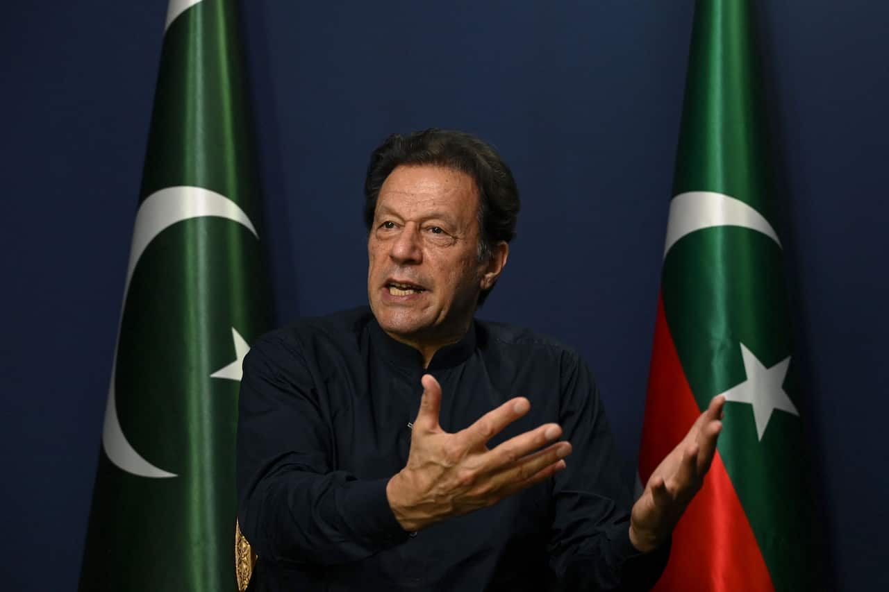Imran Khan gesturing and speaking in between two flags.