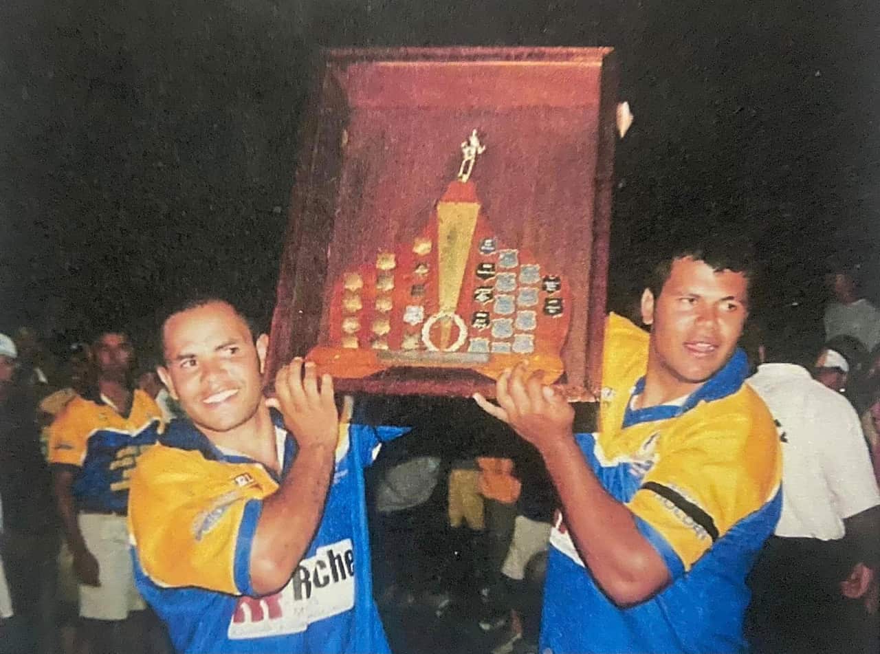 Two man standing smiling holding a premiership trophy
