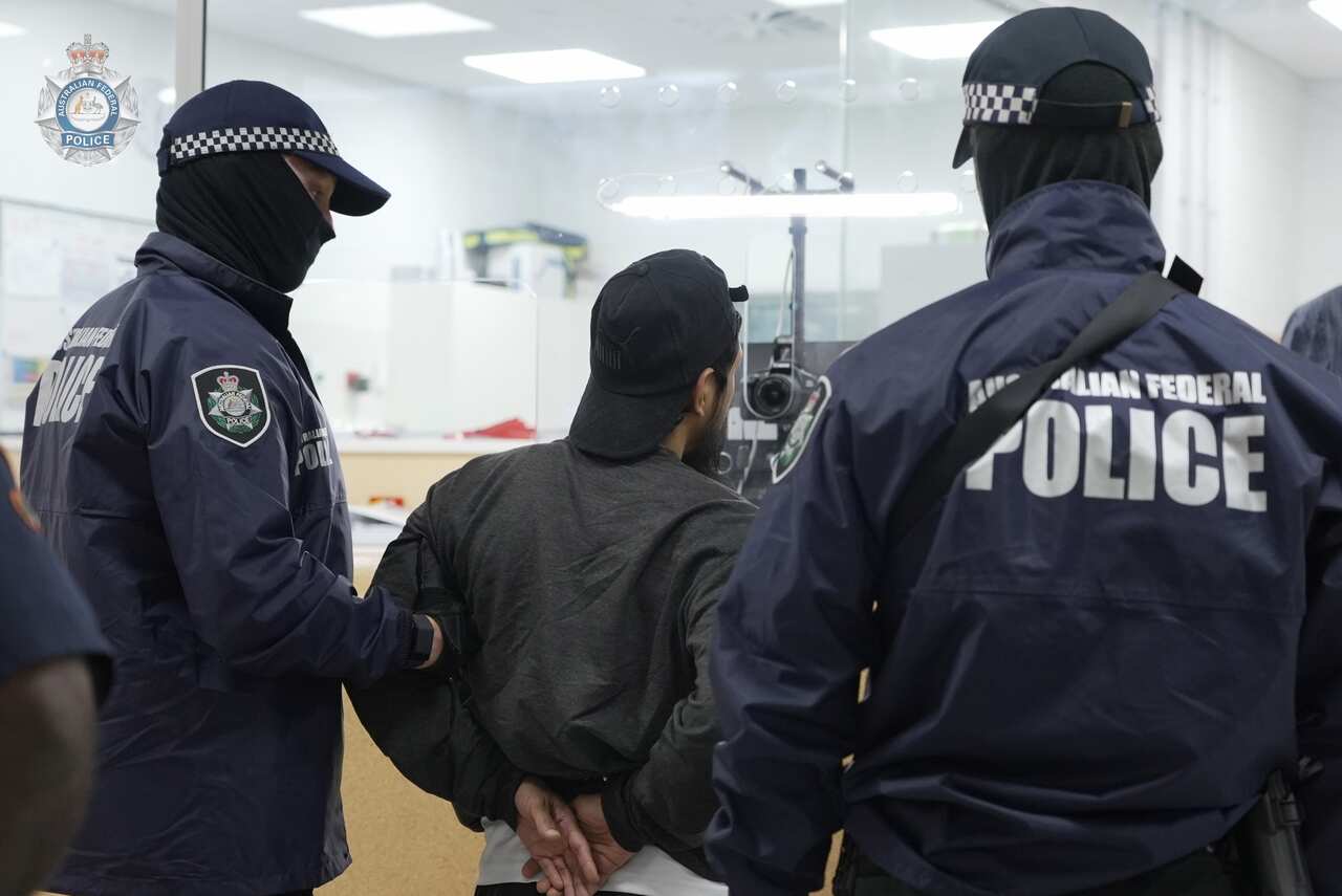 A man in handcuffs stands between two AFP officers.
