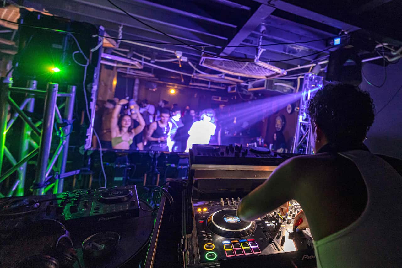 A woman operating audio equipment at a venue as people dance in front of her.