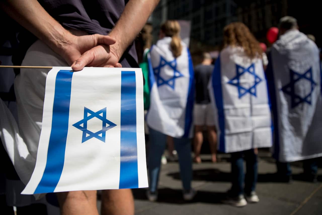 A person holding an Israeli flag behind them and others wearing the flags as capes.