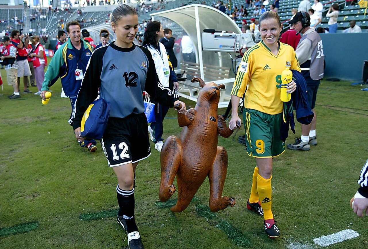 Two Australian female football  players approach the bench holding a blow up kangaroo.