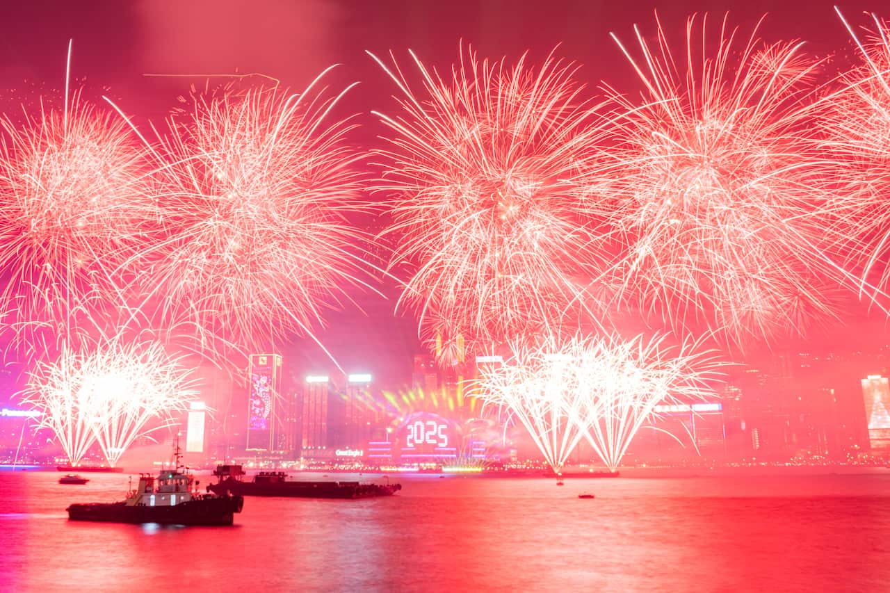 A fireworks display lights up the sky above a harbour with boats sailing in the foreground.