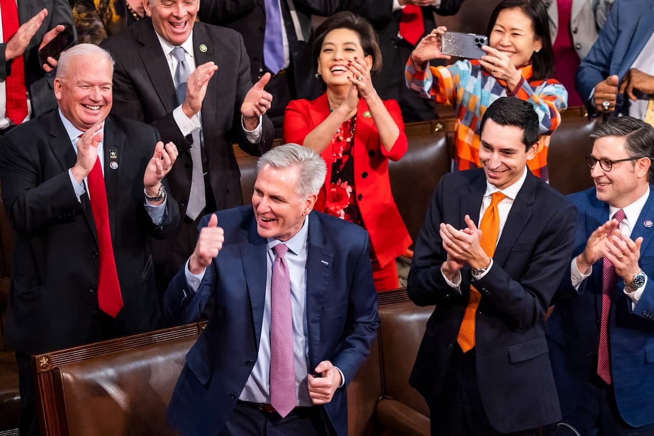 A man wearing a suit gestures as he is surrounded by colleagues in the US House of Representatives.