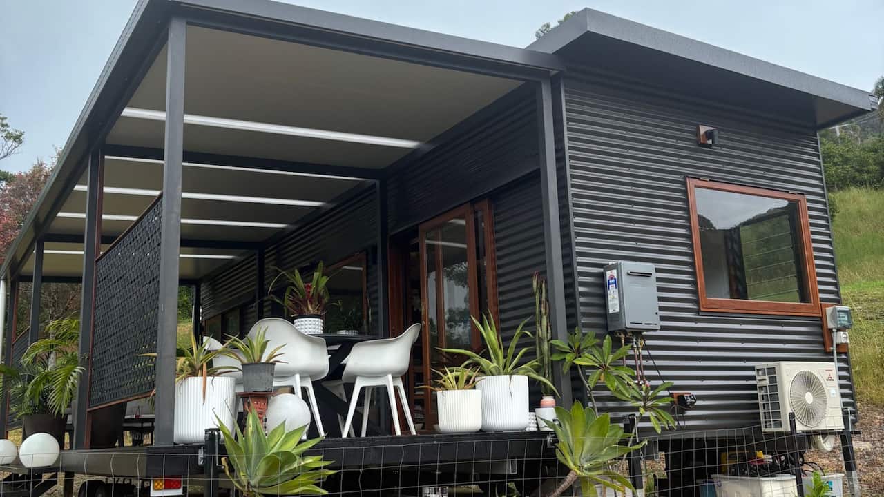 a grey colourbond tiny home with wooden edges and plants on balcony