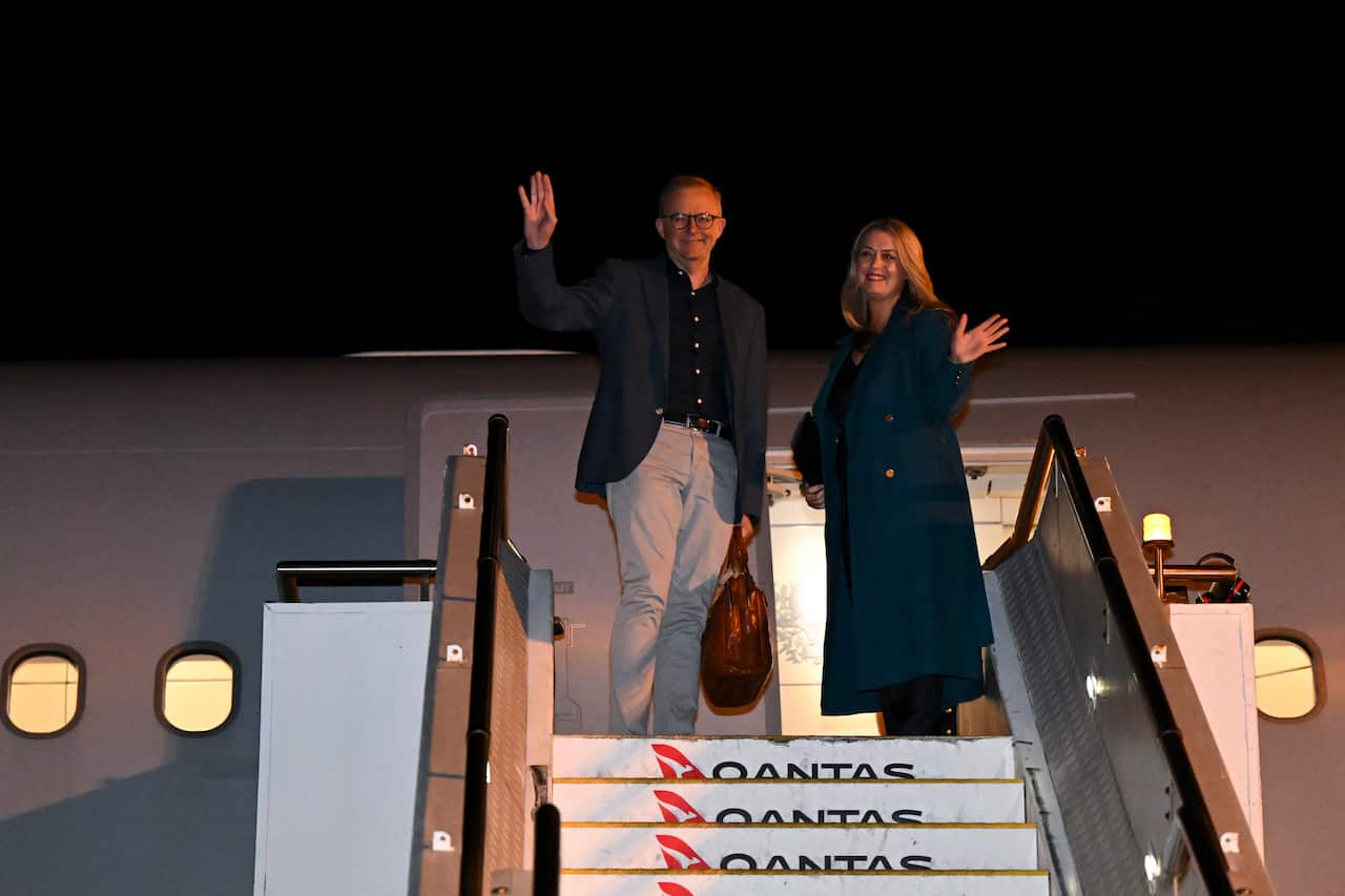 Anthony Albanese and partner Jodie Haydon wave from aeroplane steps. 