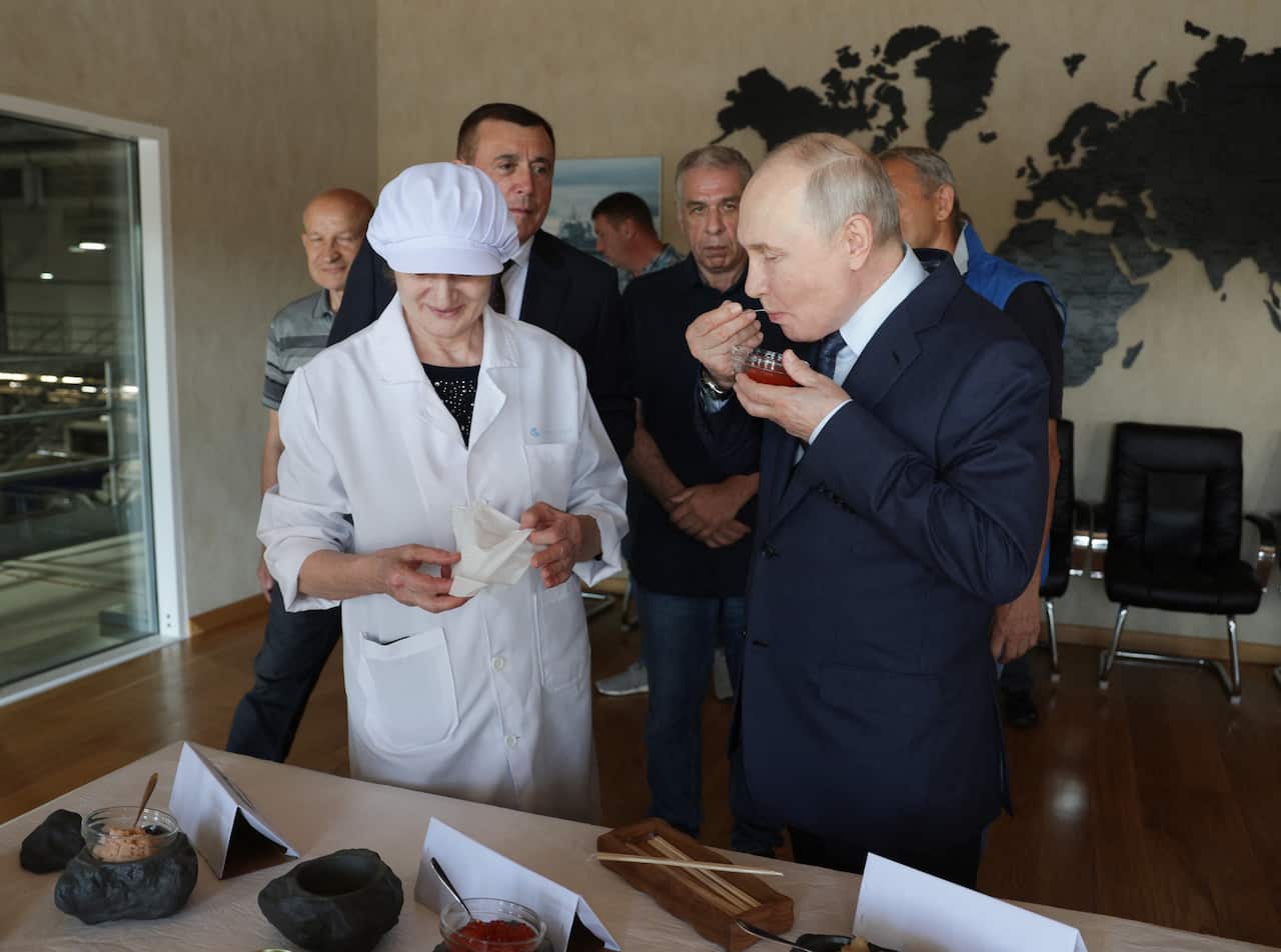 Putin eats caviar in an administrative room with people looking on.