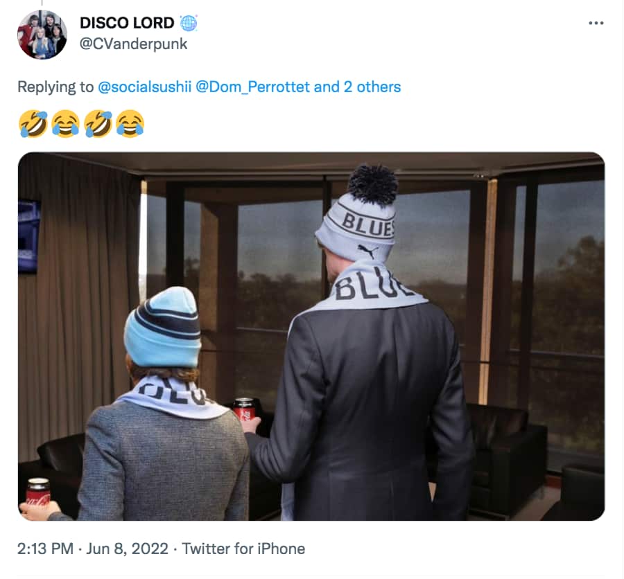 A woman and a man in matching beanies and scarfs stand side by side holding a can of soft drink.