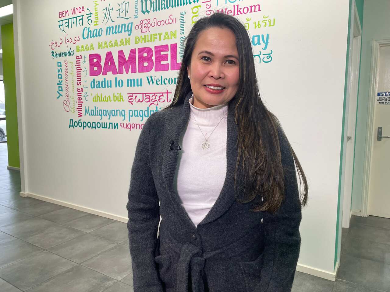 A Filipino woman standing in front of a wall with the word 'Welcome' painted in multiple languages.