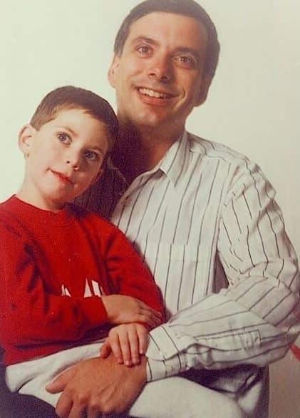 A man sits with a young boy on his lap. They are both smiling.