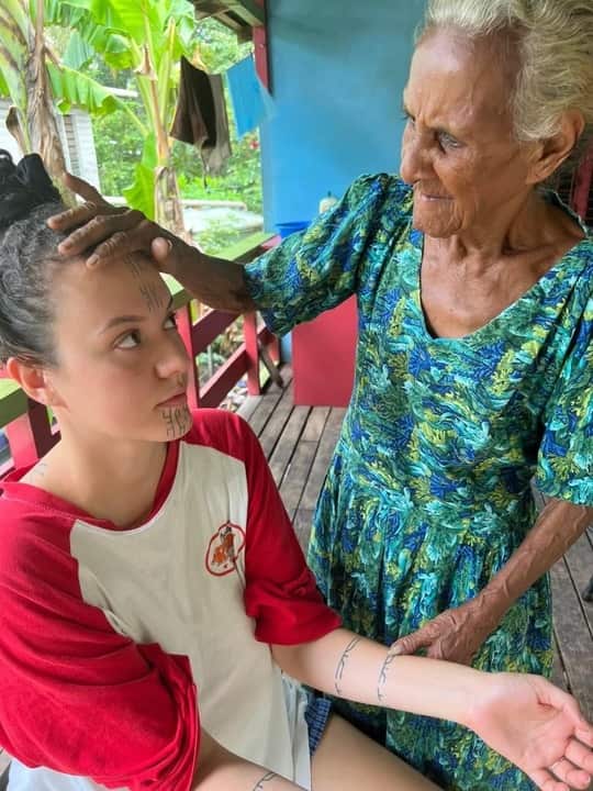 An elderly woman looks at a younger woman's cultural face markings.
