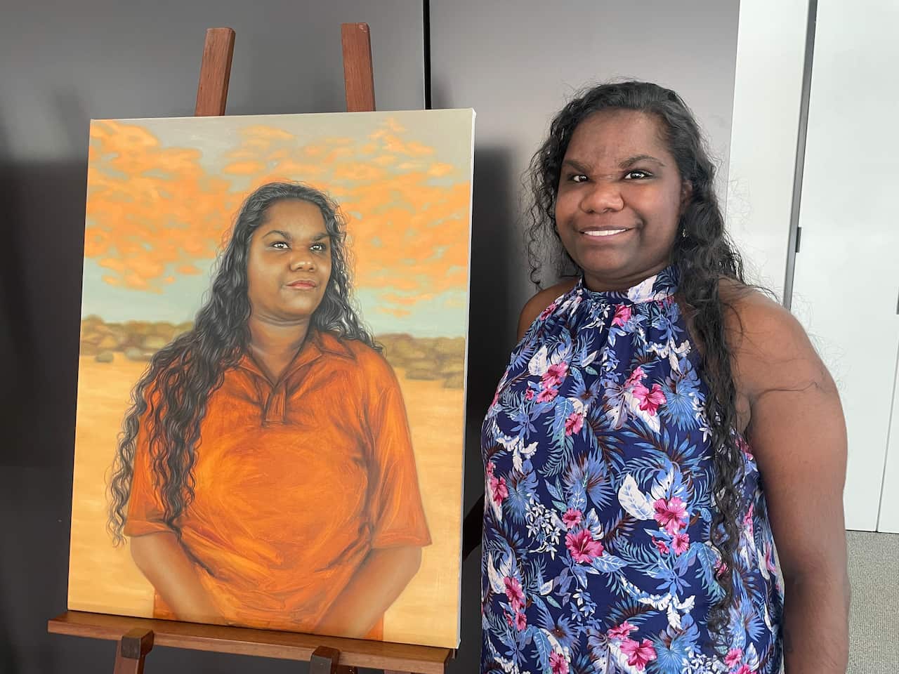 A woman smiling next to a portrait of her.