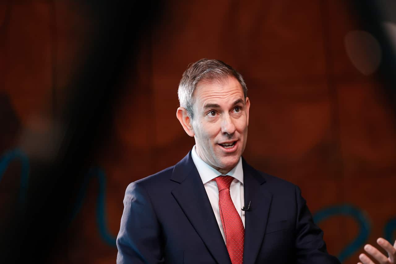 A man in a navy suit and red tie speaking.