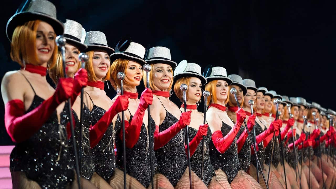 A line up of cabaret dances stand with top hats and a cane