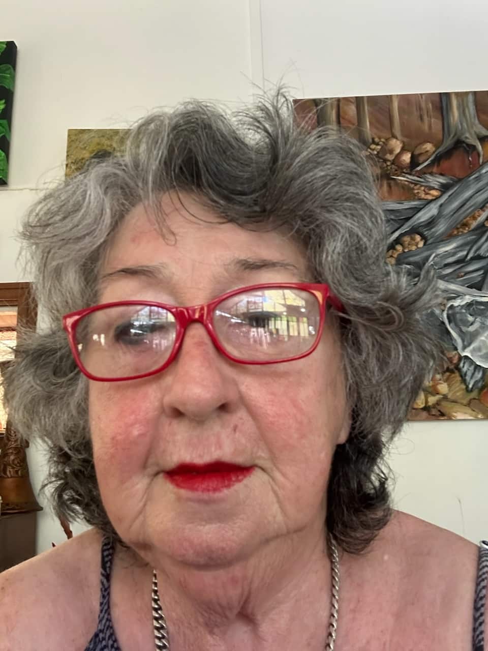 A selfie of a woman with short grey hair and red lipstick looking at the camera with a neutral expression.