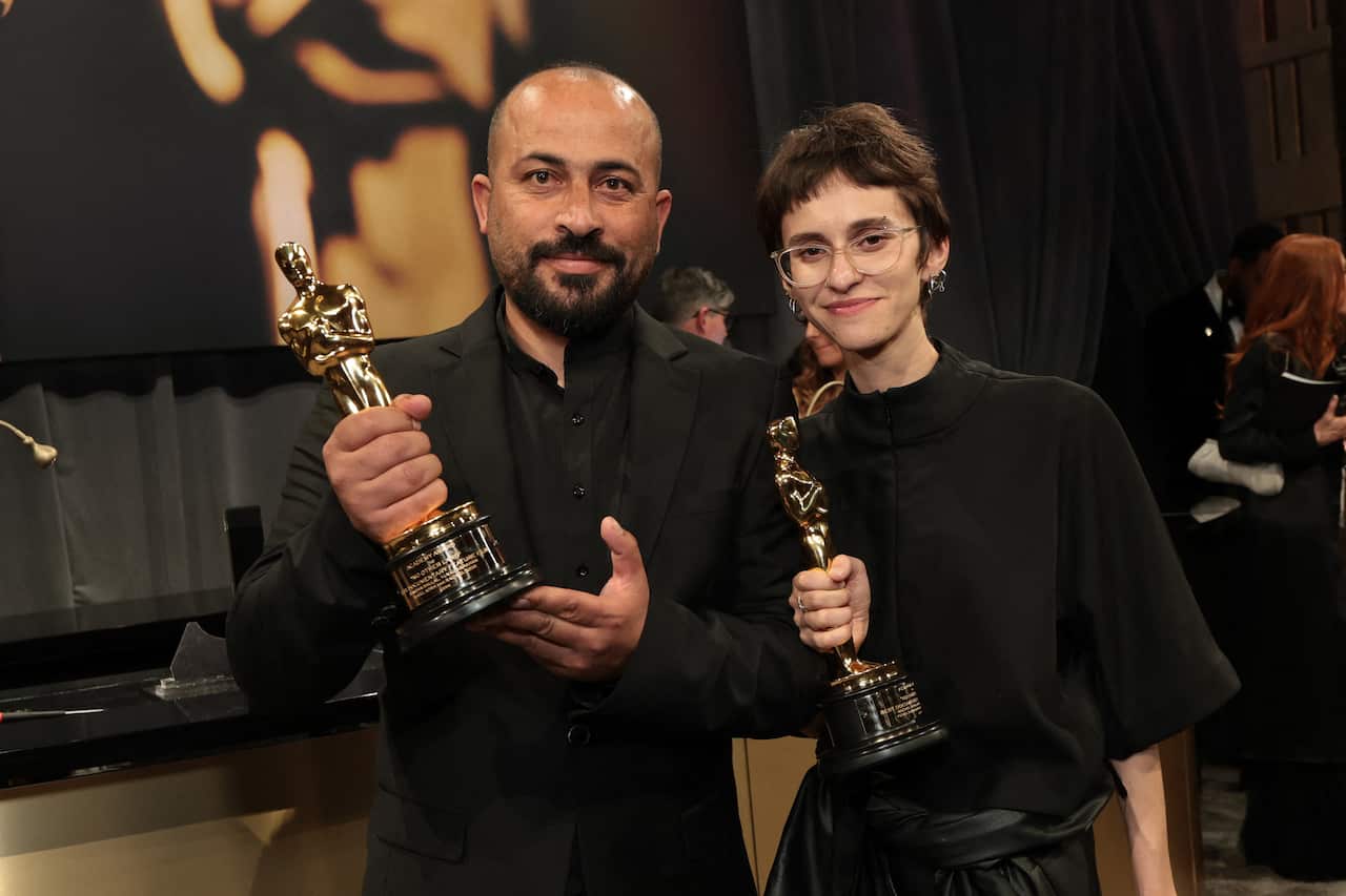 A man and a woman pose for a photo, both holding Oscar trophies in their hands