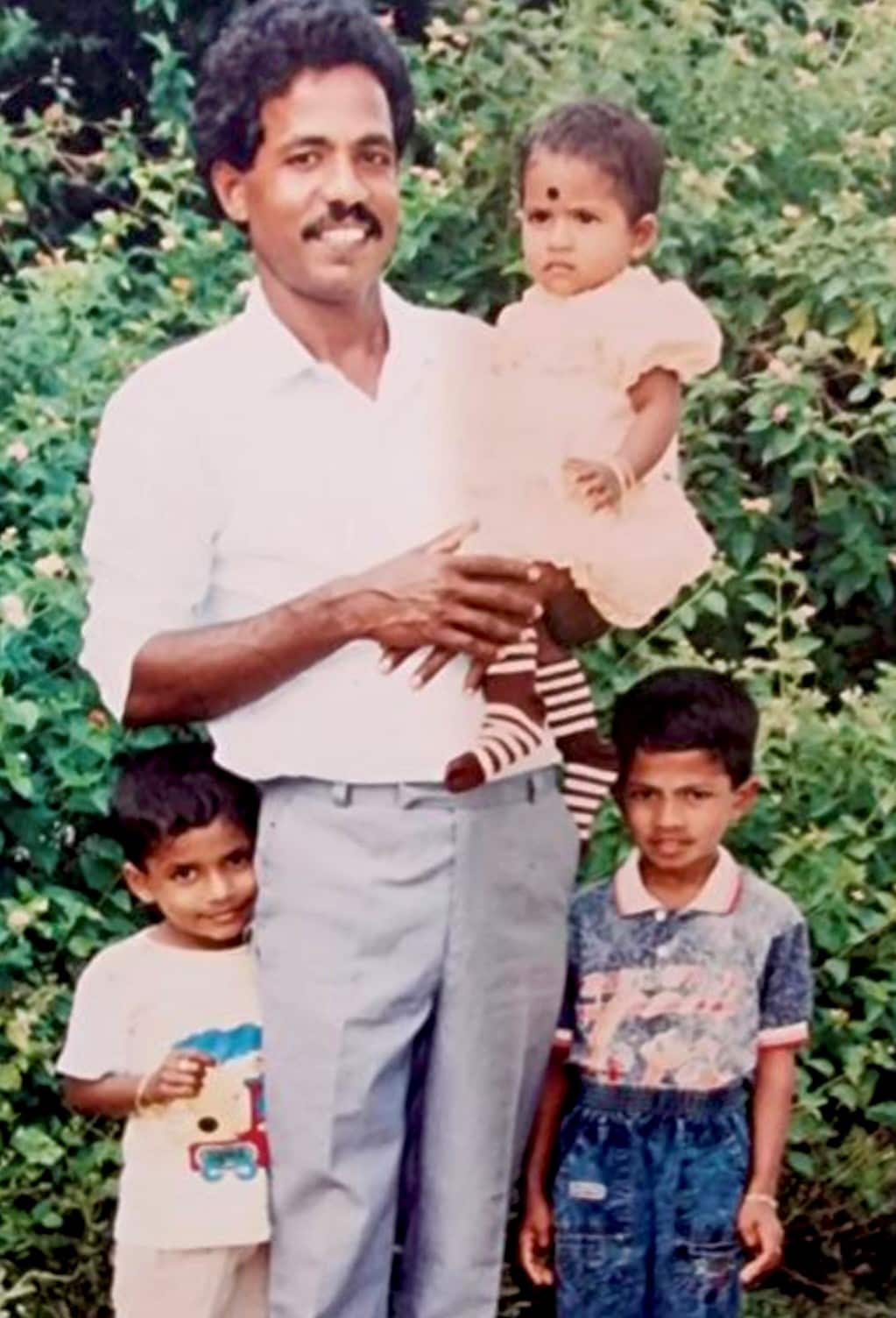 A Sri Lankan man holding a young girl in an apricot dress with two small boys standing beside him.