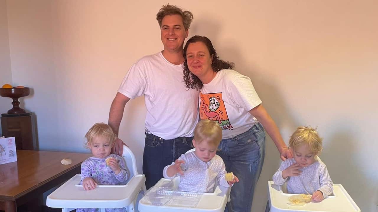 three baby girls in highchairs eating and their mum and dad standing behind them