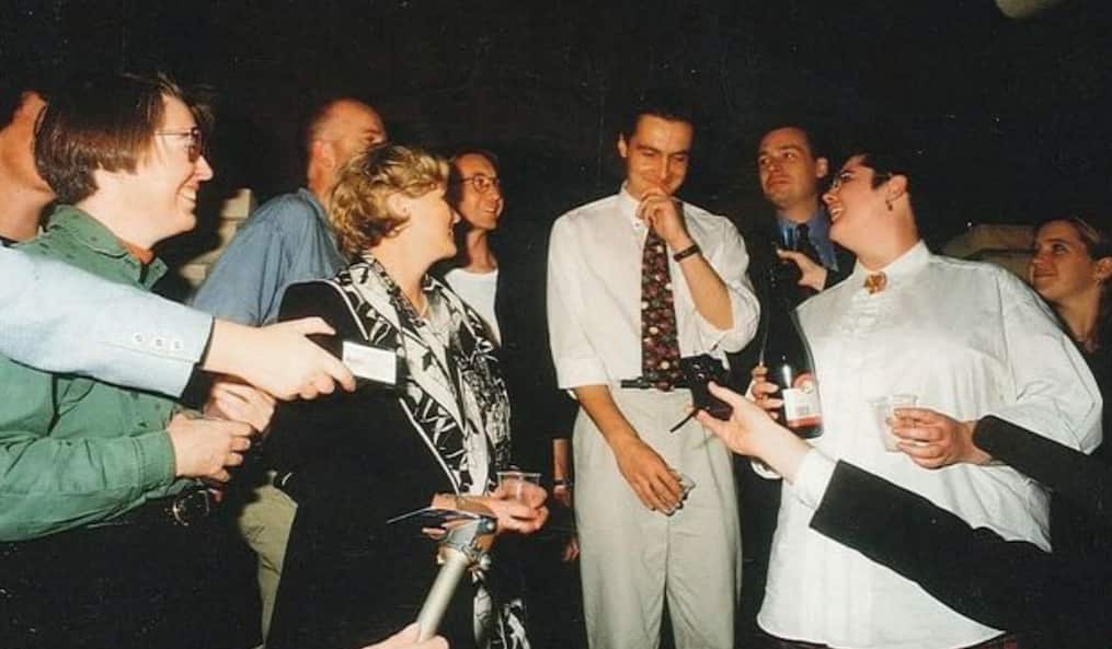 Man smiling, surrounded by microphones and dictaphones. 