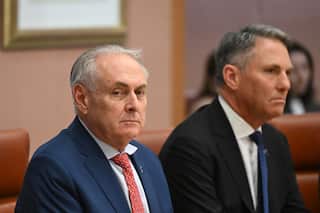Two older white men in suits sit beside each other looking serious.