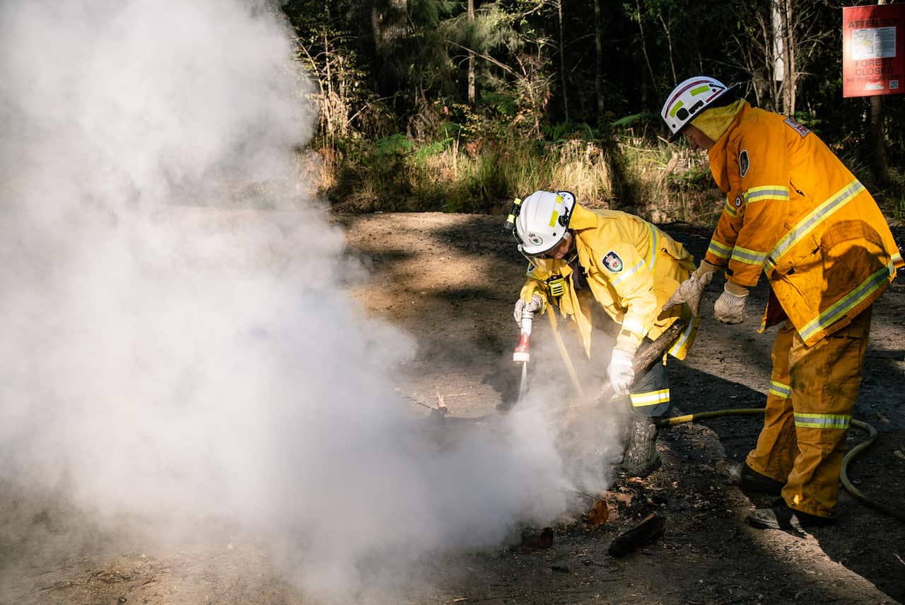 fire officers douse a fire on a dirt road amongst a forest