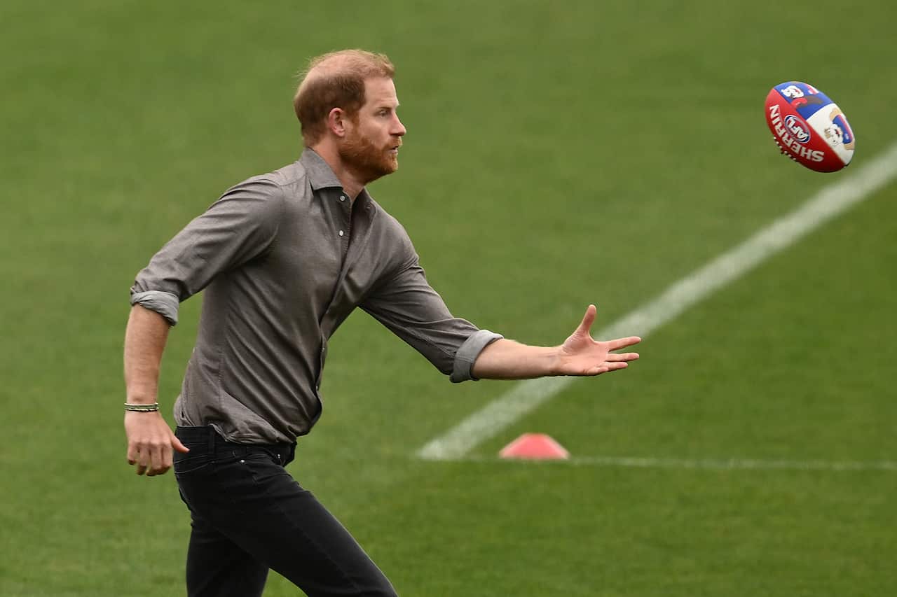 A younger white man with red hair and his arm outstretched to catch an AFL ball