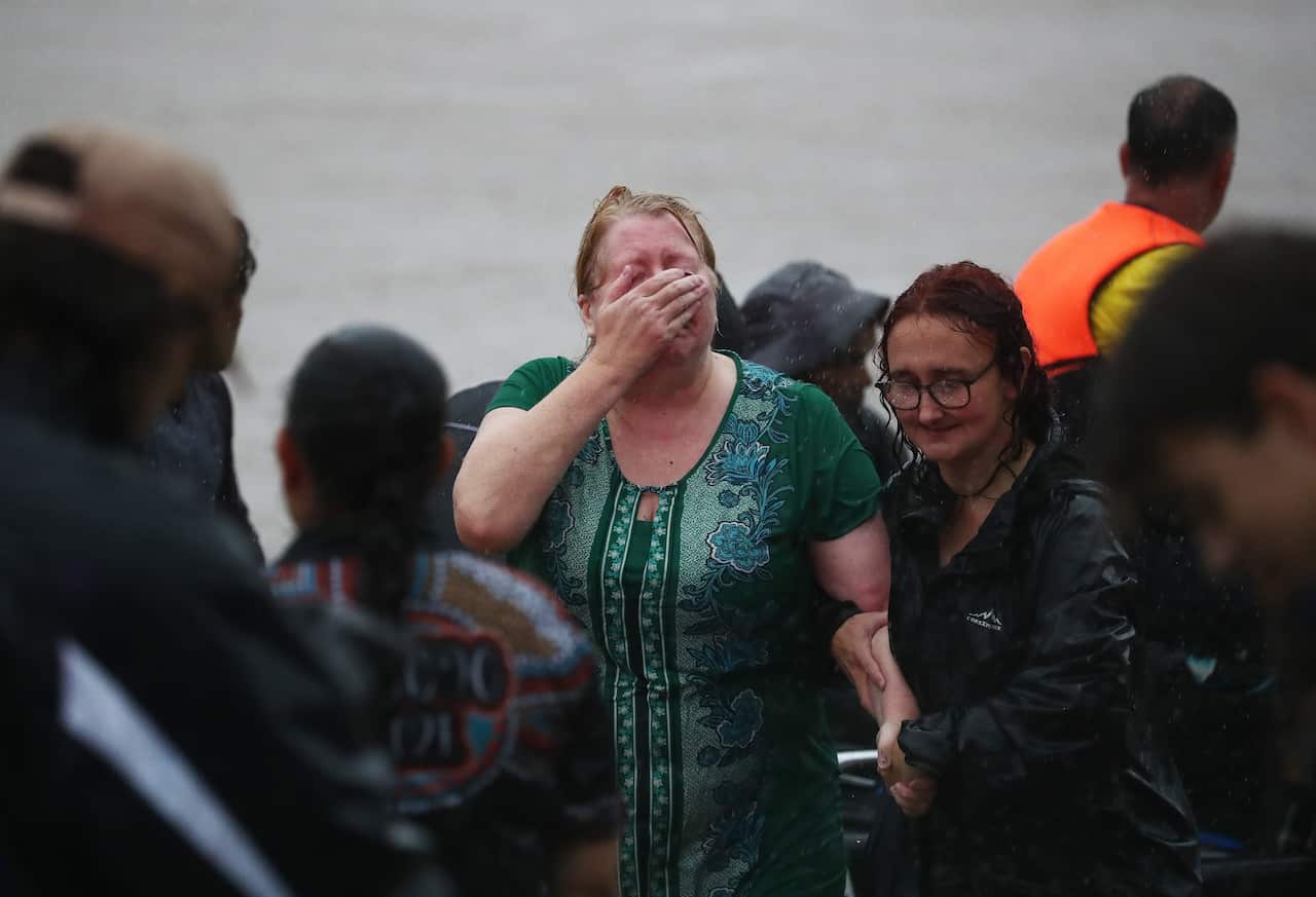 A woman clutches her face crying, accompanied by another woman holding her arm in front of flood waters. 