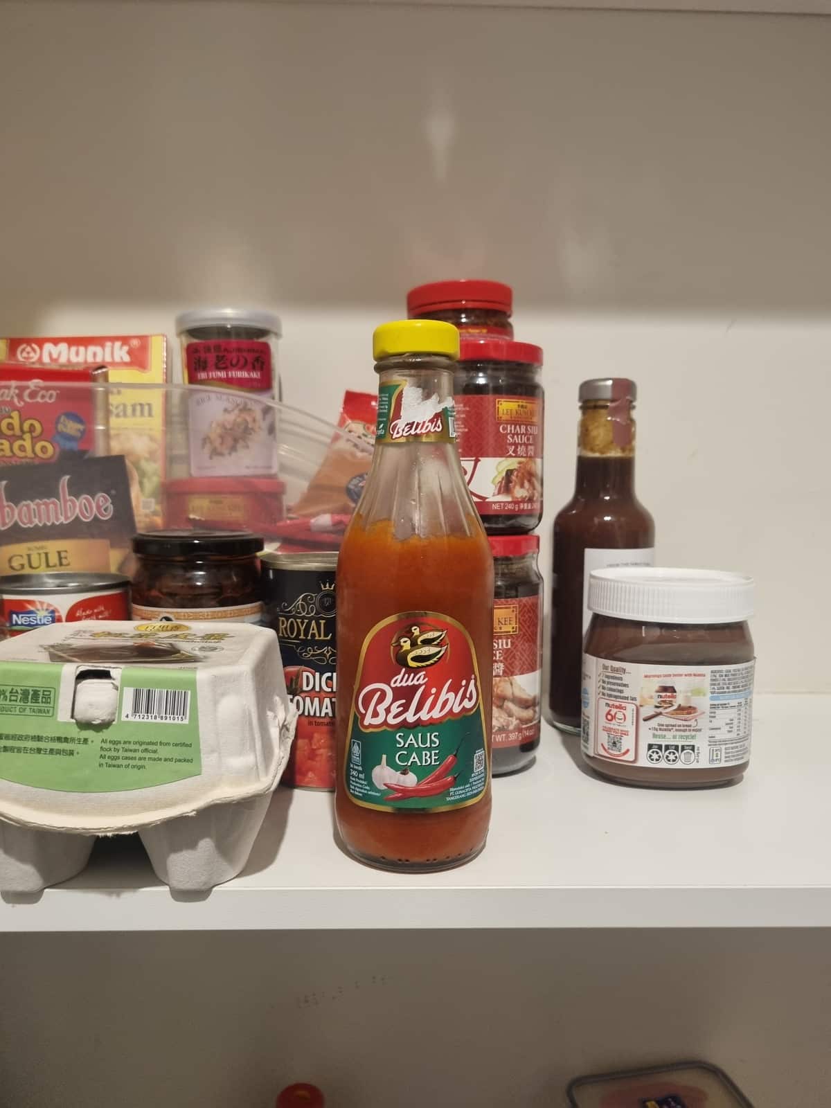 Belibis hot sauce surrounded by other condiments on a white shelf.