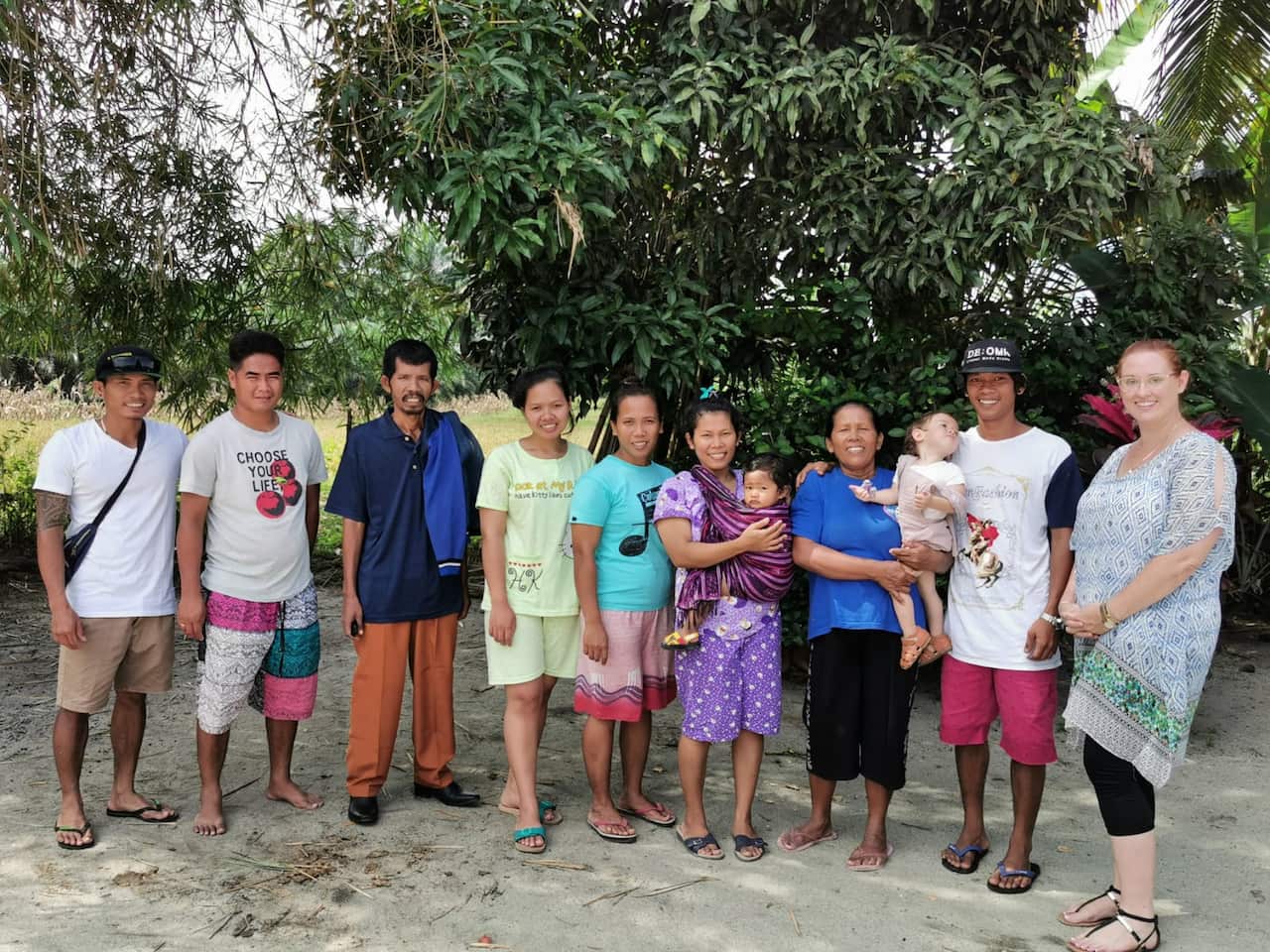 Nine adults standing in a line on a beach. Two women are holding young children.