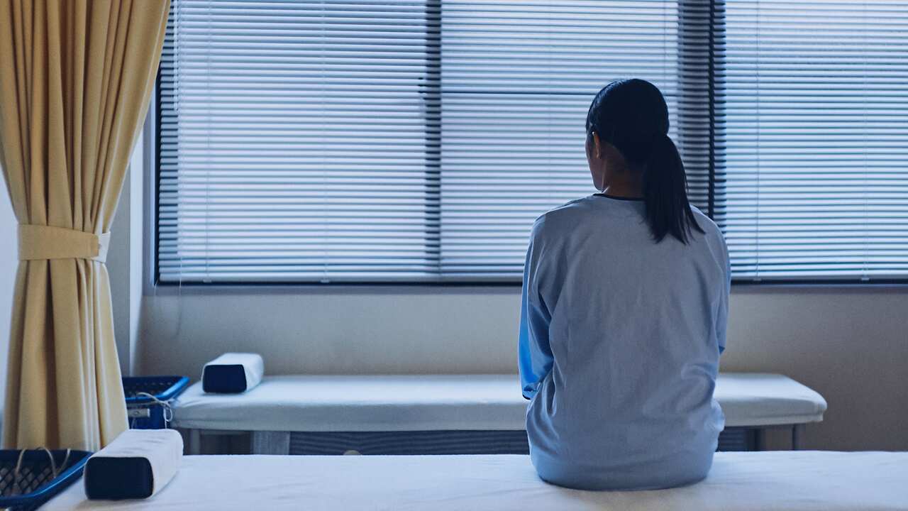 Woman sitting on a hospital bed facing away from the camera.
