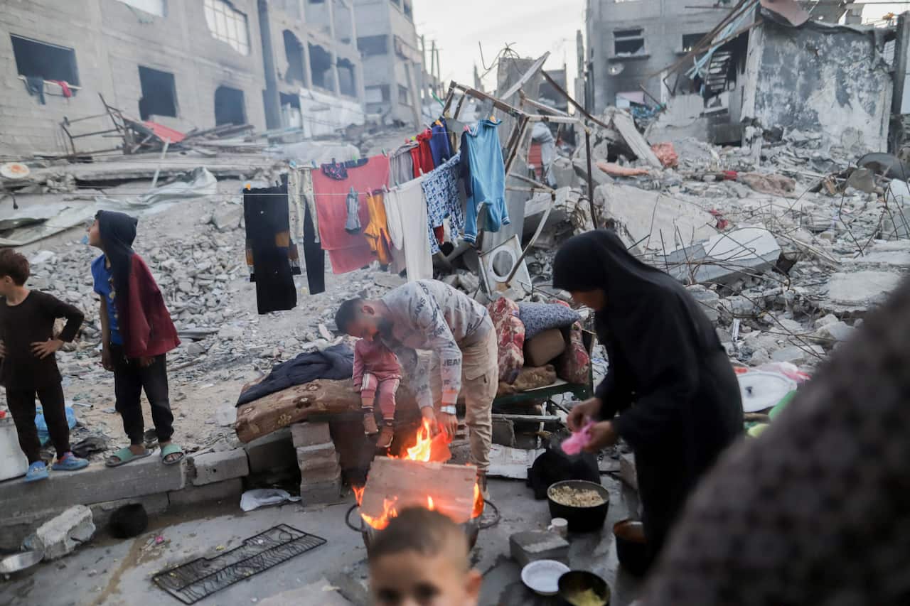 A woman cooking food over a small fire among debris and demolished buildings.