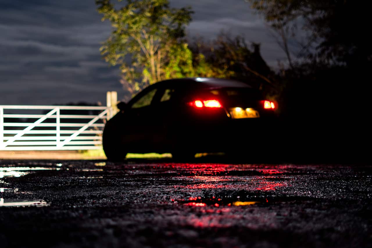 A low angle, shallow depth of field shot of a black sinister car, parked by a gate in the countryside at night
