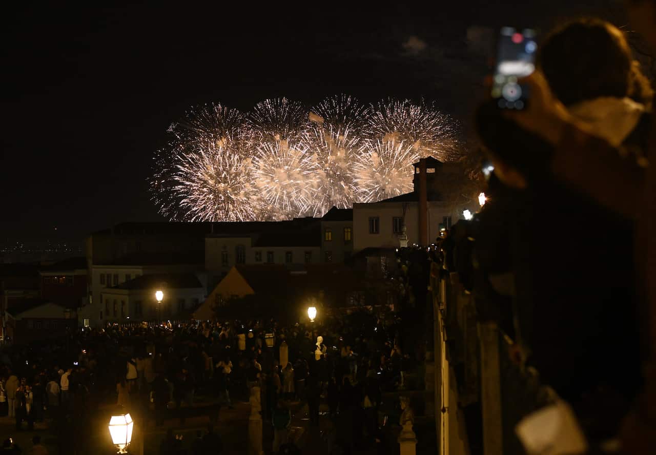 Fireworks over a city with crowds of people in the street.