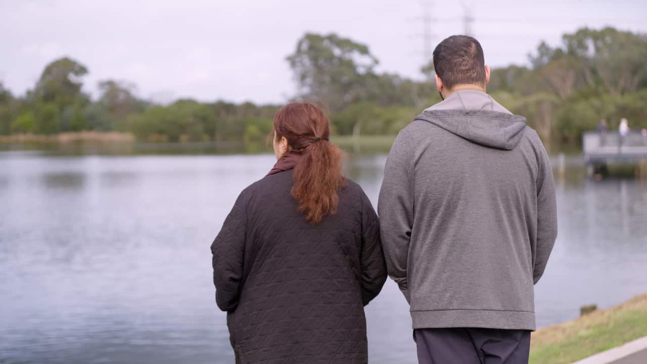 Rear view of an adult boy standing next to his mum next to a large lake.
