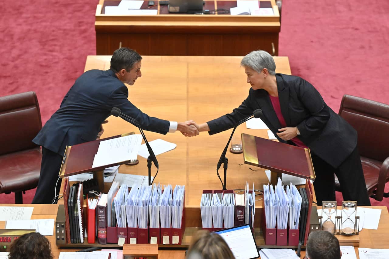 Two people lean across a table to shake hands.