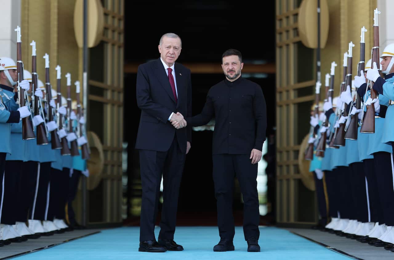Recep Tayyip Erdogan and Volodymyr Zelenskyy stand together shaking hands posing for a photograph surrounded by guards.