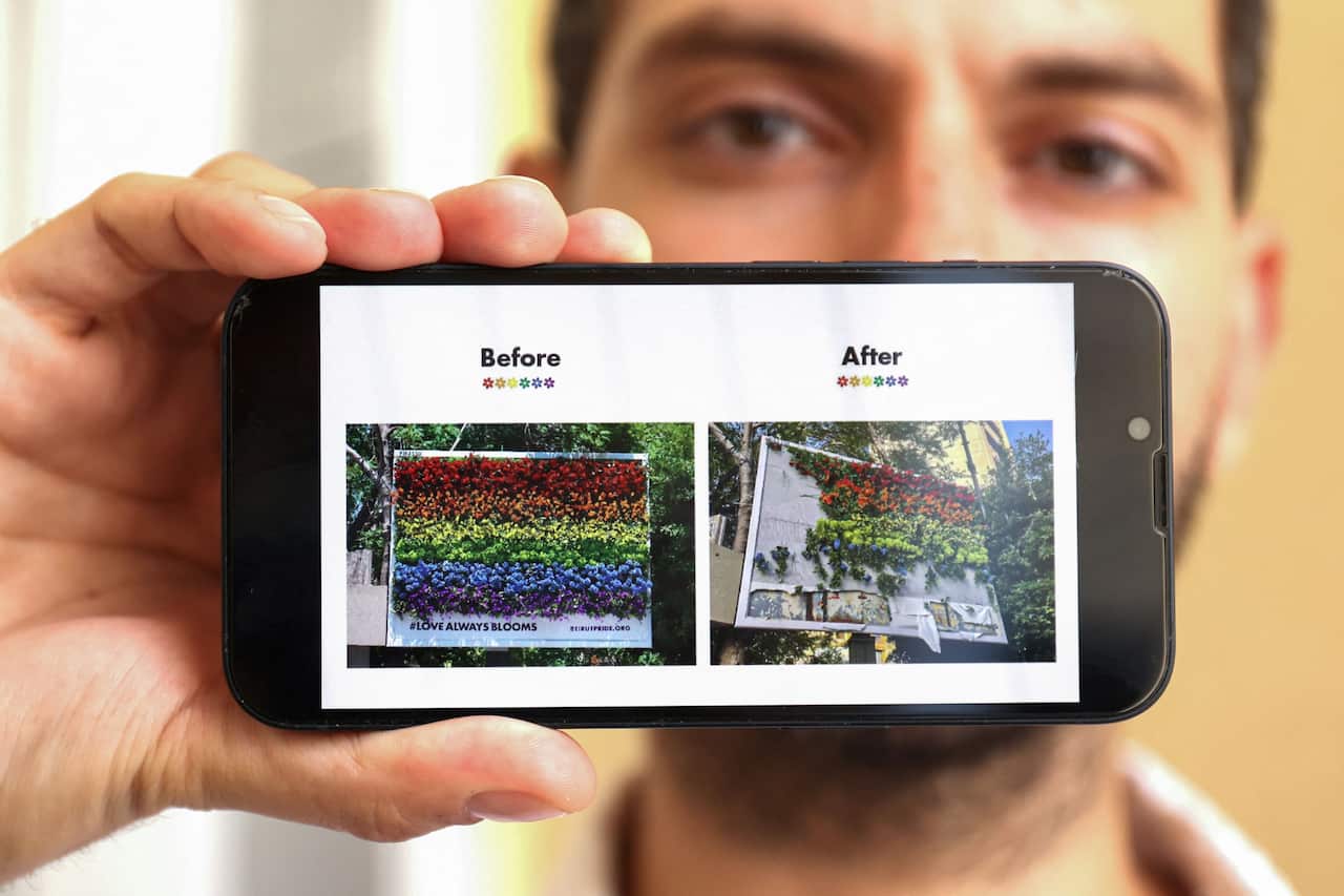 A man shows pictures on his telephone of a billboard featuring blooming flowers in the colours of a rainbow flag