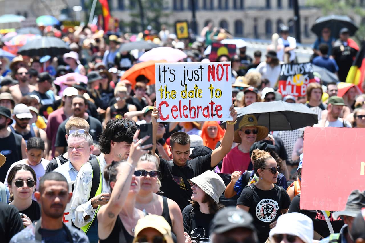 People march in an Invasion Day rally. One holds up a sign reading "It's just not the date to celebrate".