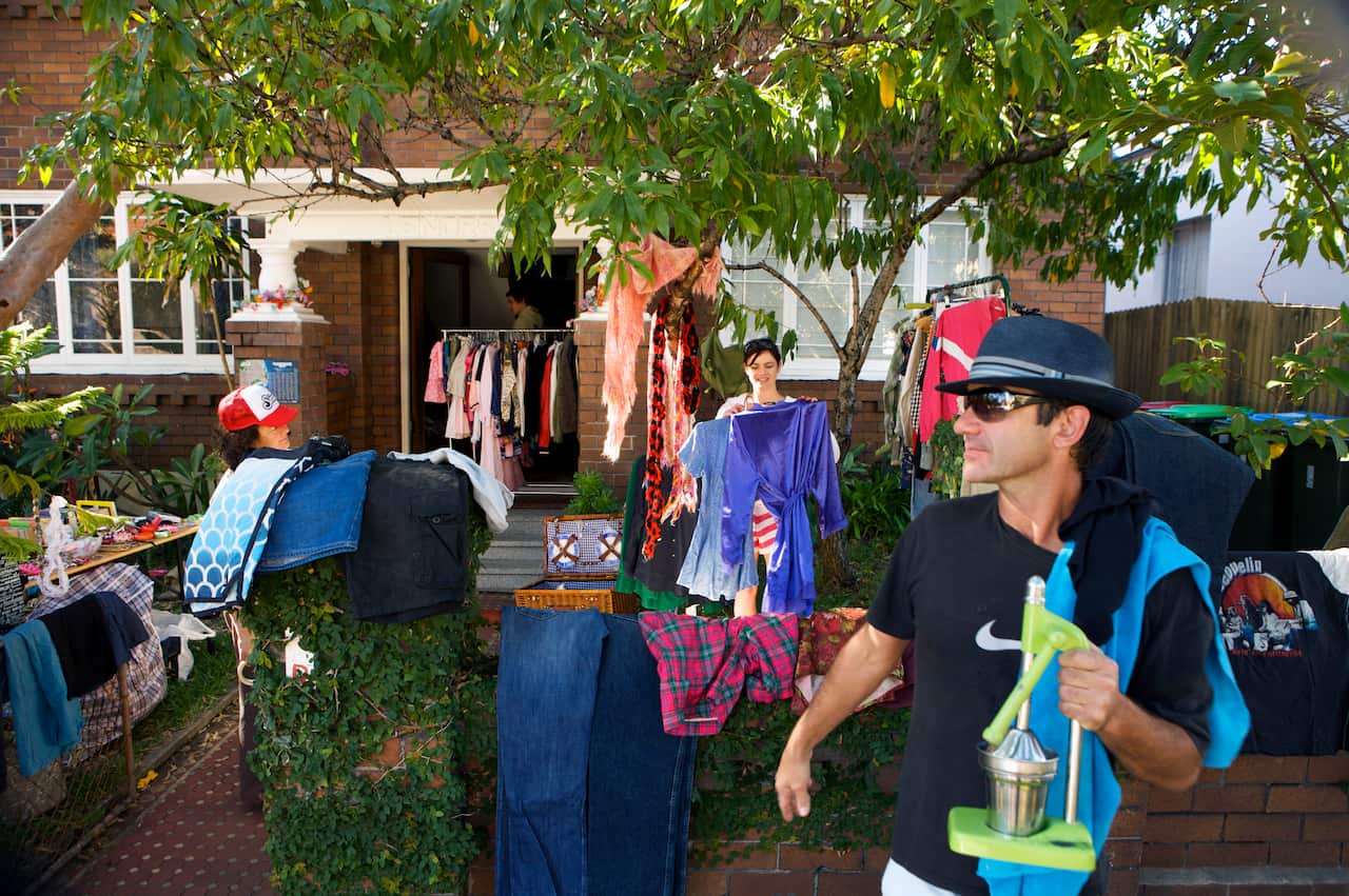 People sort through clothes and other items at a garage sale in the front yard of a brick house.