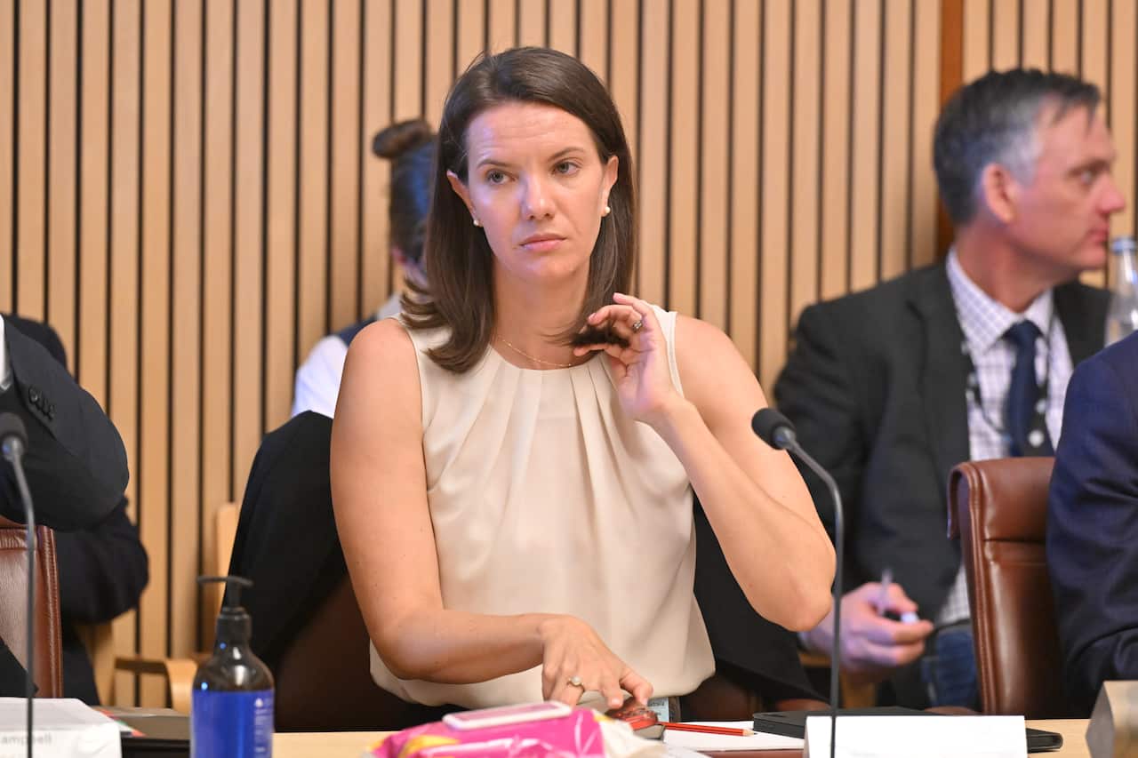 A woman sits at a table with a microphone in front of her