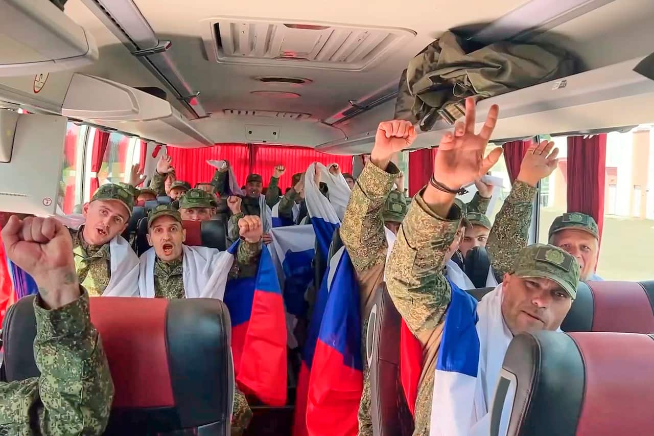 Men in fatigue sitting in a bus with their hands raised in a victory sign.