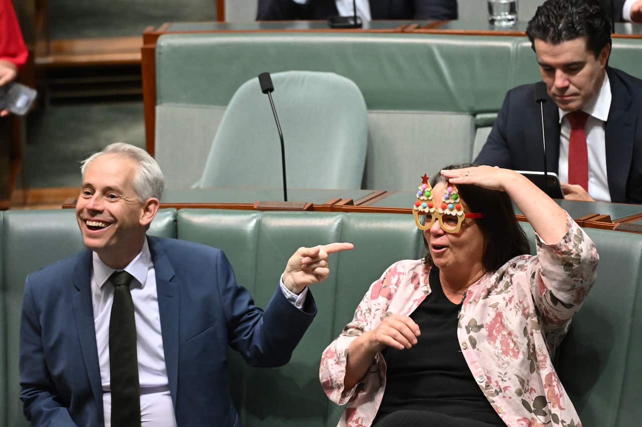 A man in a suit smiles as he points his finger at a woman sitting next to him wearing funny glasses.