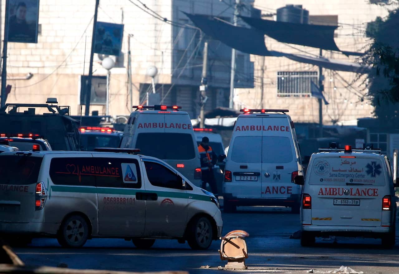 Four ambulances drive through a dusty and congested street 