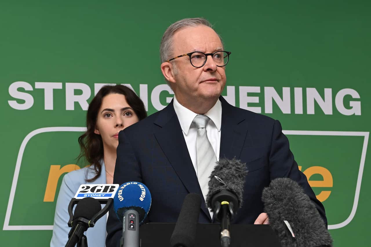 Anthony Albanese is speaking into microphones in front of a green background.