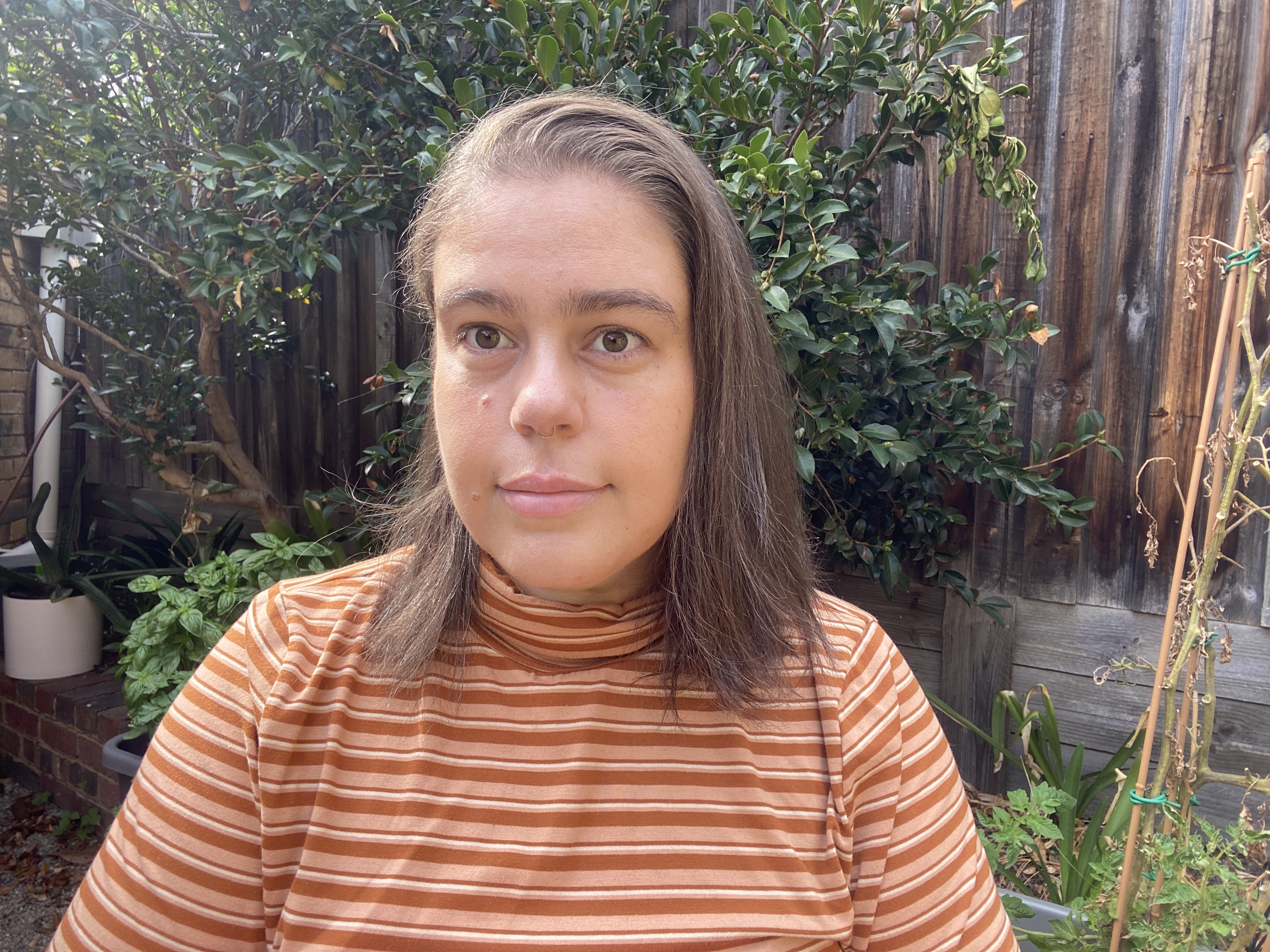 a closeup on a young woman with brown bob and wearing an orange-and-brown horizontally striped skivvy in a backyard