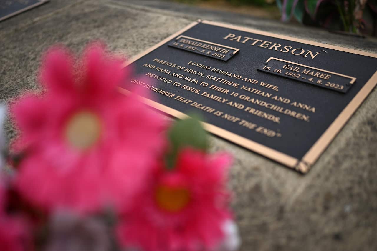 A gravestone with two names on it is seen with flowers in the foreground.