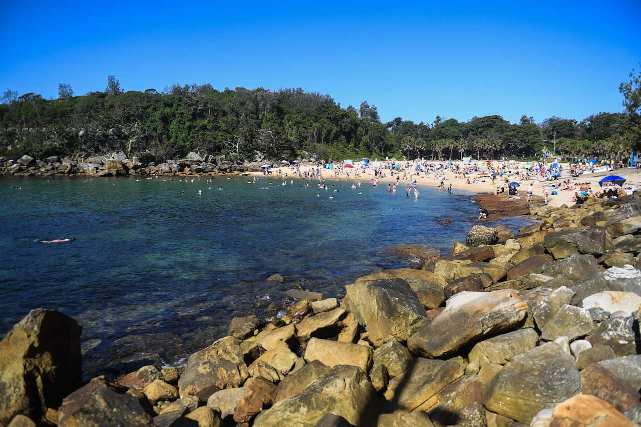People at a beach in the mid-distance. There are rocks and water in the foreground