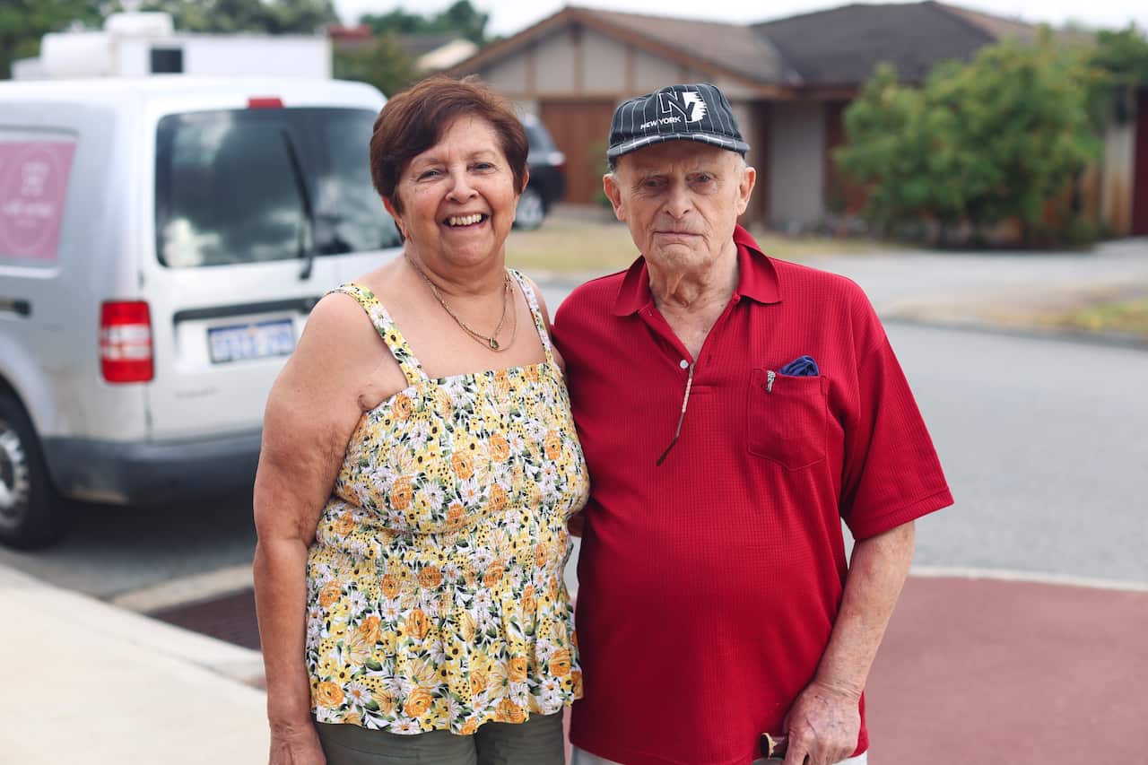 A woman wearing a floral top and man wearing a red shirt pose for a photo.