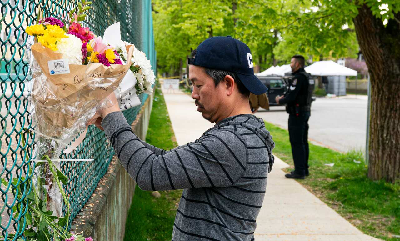 A man is leaving flowers on a fence.