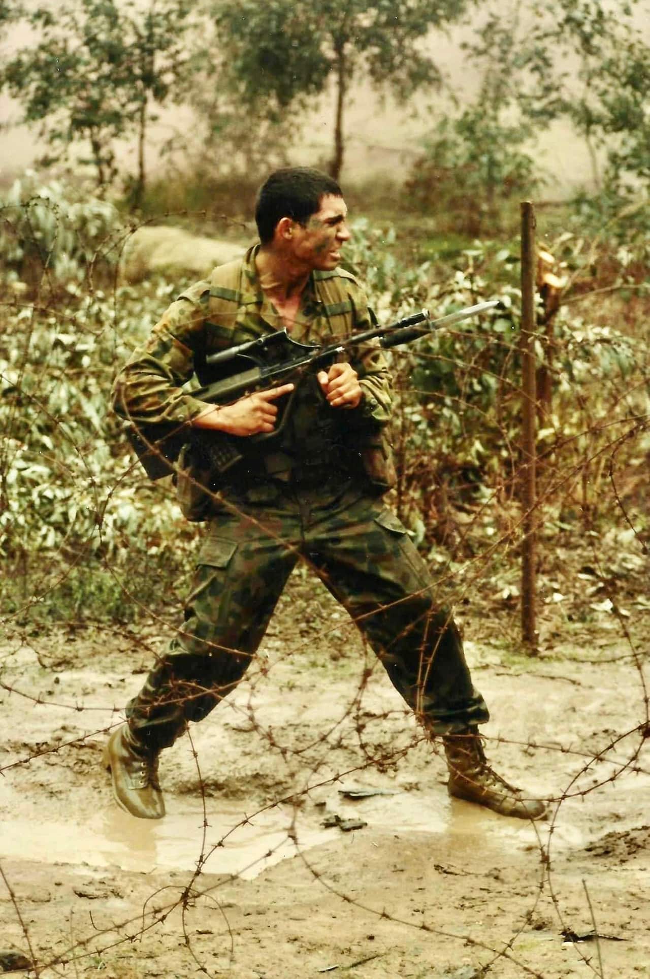 Paul walker in uniform carrying a gun with bayonet standing in a muddy road before barbed wire